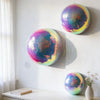 A set of iridescent disco balls mounted on a white wall, featuring various shades of purple, blue, and green.