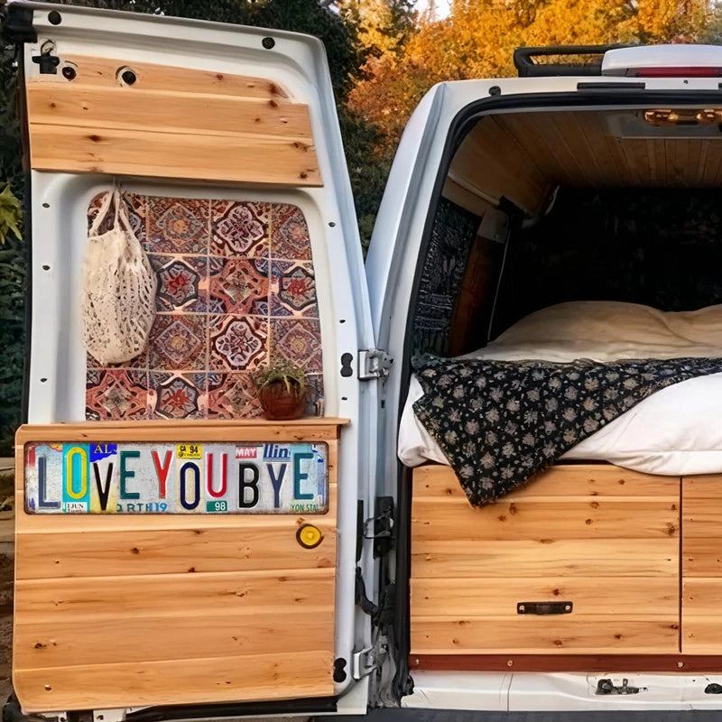 A vintage metal street sign decor is mounted on the side of a white van with wooden interior panels and a custom-built bed.