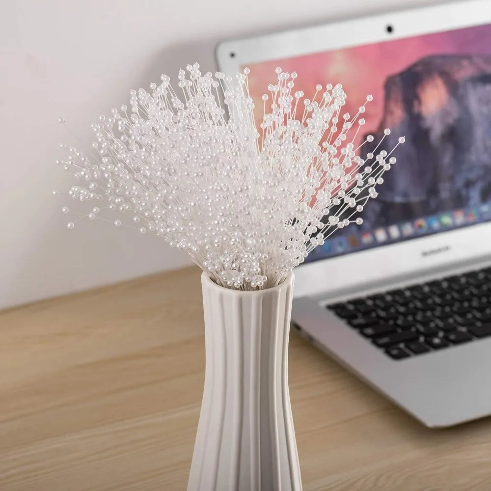 A white vase filled with pearl string beads used for weddings and DIY decor, placed in front of a laptop.