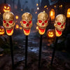 Four realistic skull solar pathway lights illuminate a dark outdoor path for Halloween decorations.
