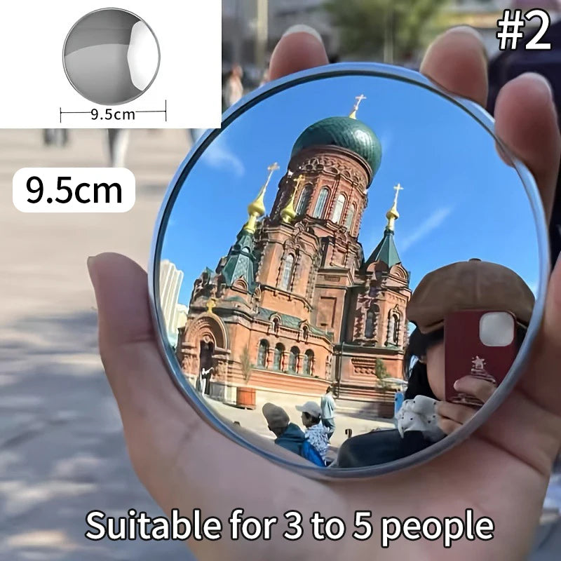 A round convex mirror is held in a hand, reflecting a large cathedral and people.