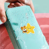 A hand is applying a clear printable vinyl sticker paper featuring a yellow star-shaped cat sticker onto a pink surface.