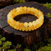 A stack of golden citrine crystal beads forming a bracelet, resting on dark wood with green moss.