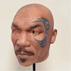 A realistic latex mask of a bald man with blue tribal markings on his face.