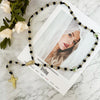 A green crystal rosary necklace featuring Saint Jude and Virgin Mary cross pendants displayed on a white card.