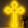 A bright yellow neon cross wall sign illuminates a textured wall, resting on a wooden surface.