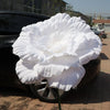 A large, white artificial peony flower is displayed on a dark car hood.