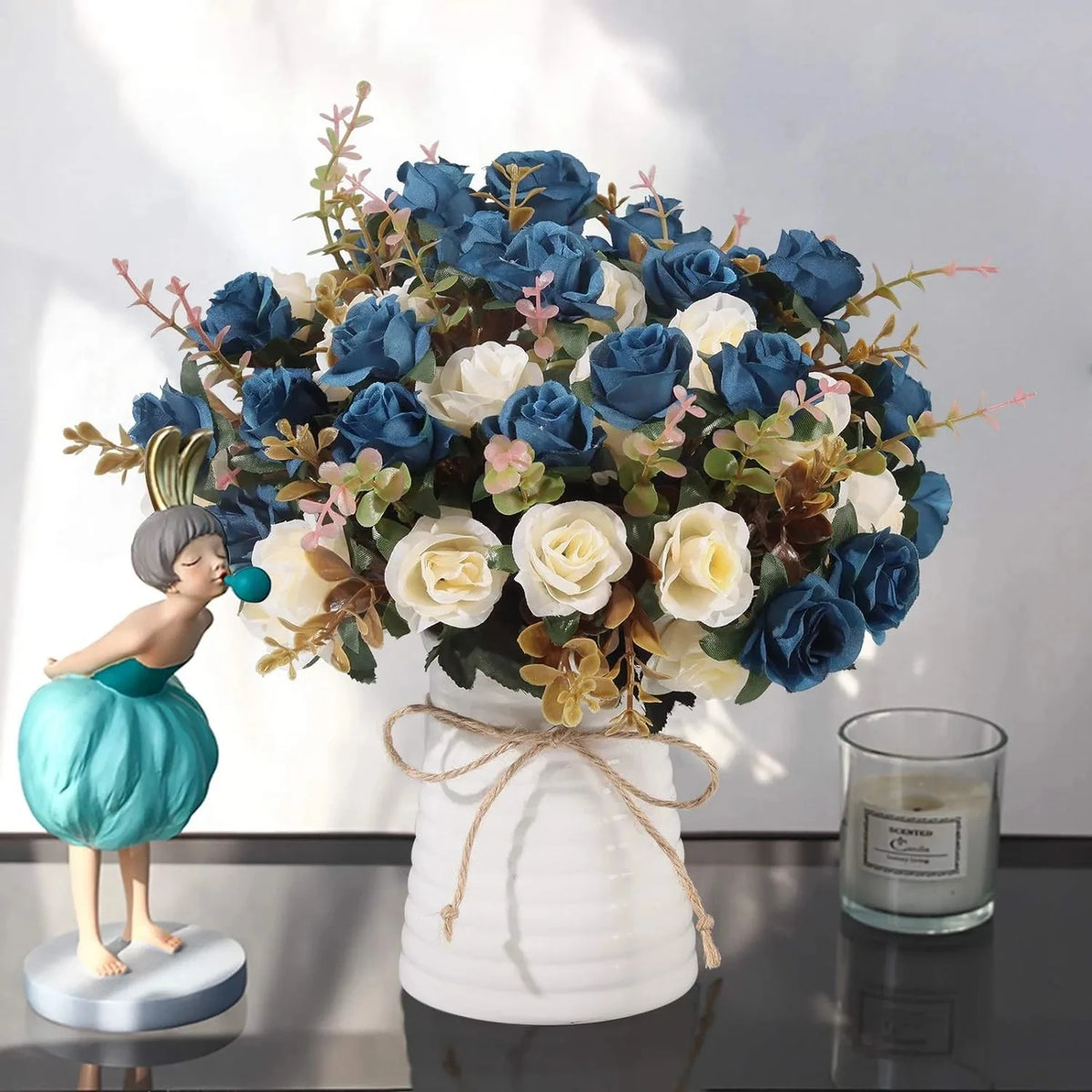 A bouquet of realistic silk blue and white roses displayed in a white vase on a dark surface.