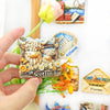 A hand holds a Scottish Highland Cow fridge magnet featuring a 3D shaggy cow with a calf, set against a white background.