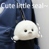 A white seal plush keychain hanging from a silver chain, displayed against a dark blue fabric.
