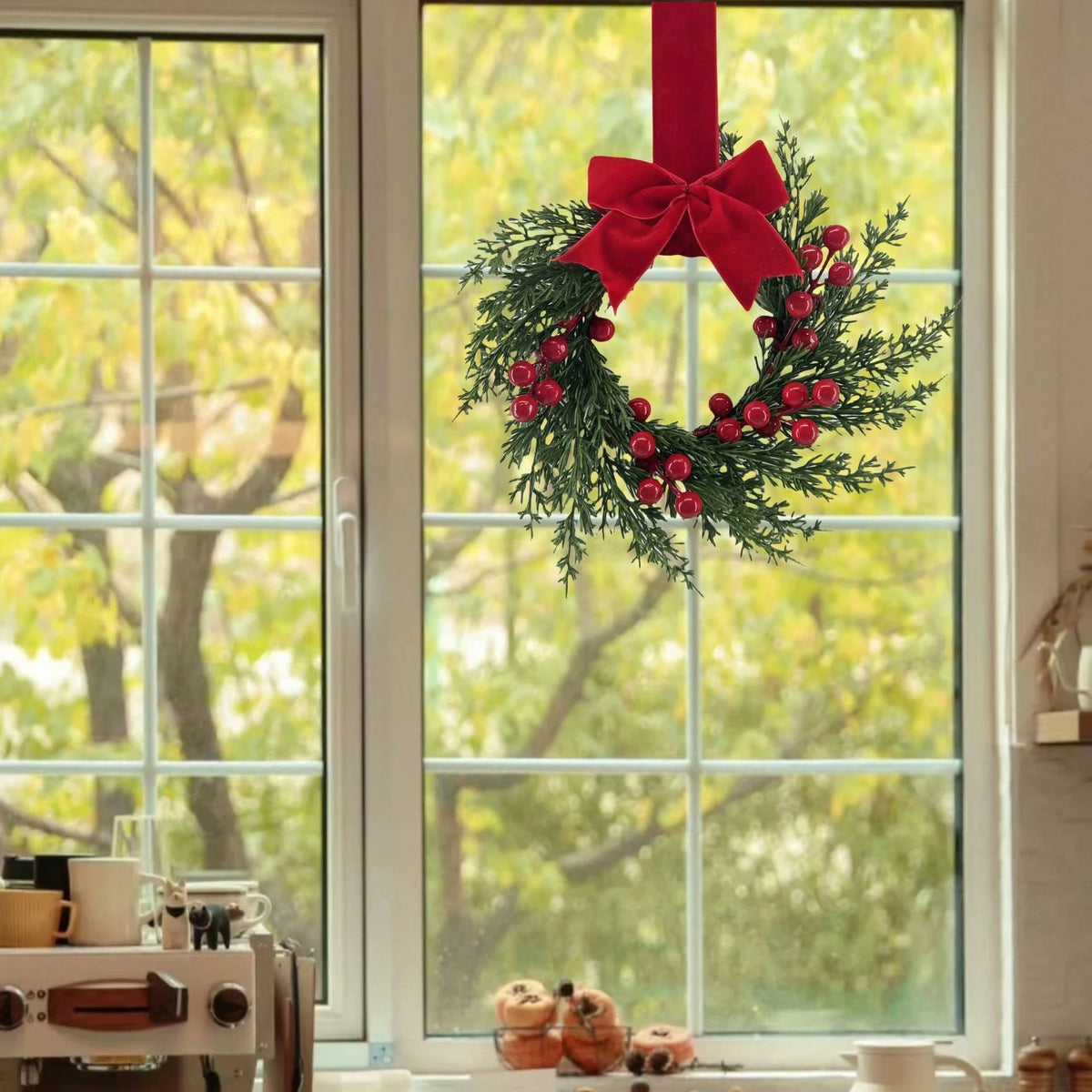 A festive Christmas wreath with red berries and a red ribbon hangs in a window.