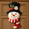A handcrafted wooden snowman decoration with a black hat, carrot nose, and red and white striped scarf hanging on a brown doo