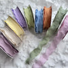 A collection of 10 yards of decorative fishtail yarn ribbon in various pastel shades including lavender, mint green, yellow, 