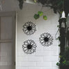 A set of black metal sunflower wall decor mounted on a white brick wall with green vines hanging above.