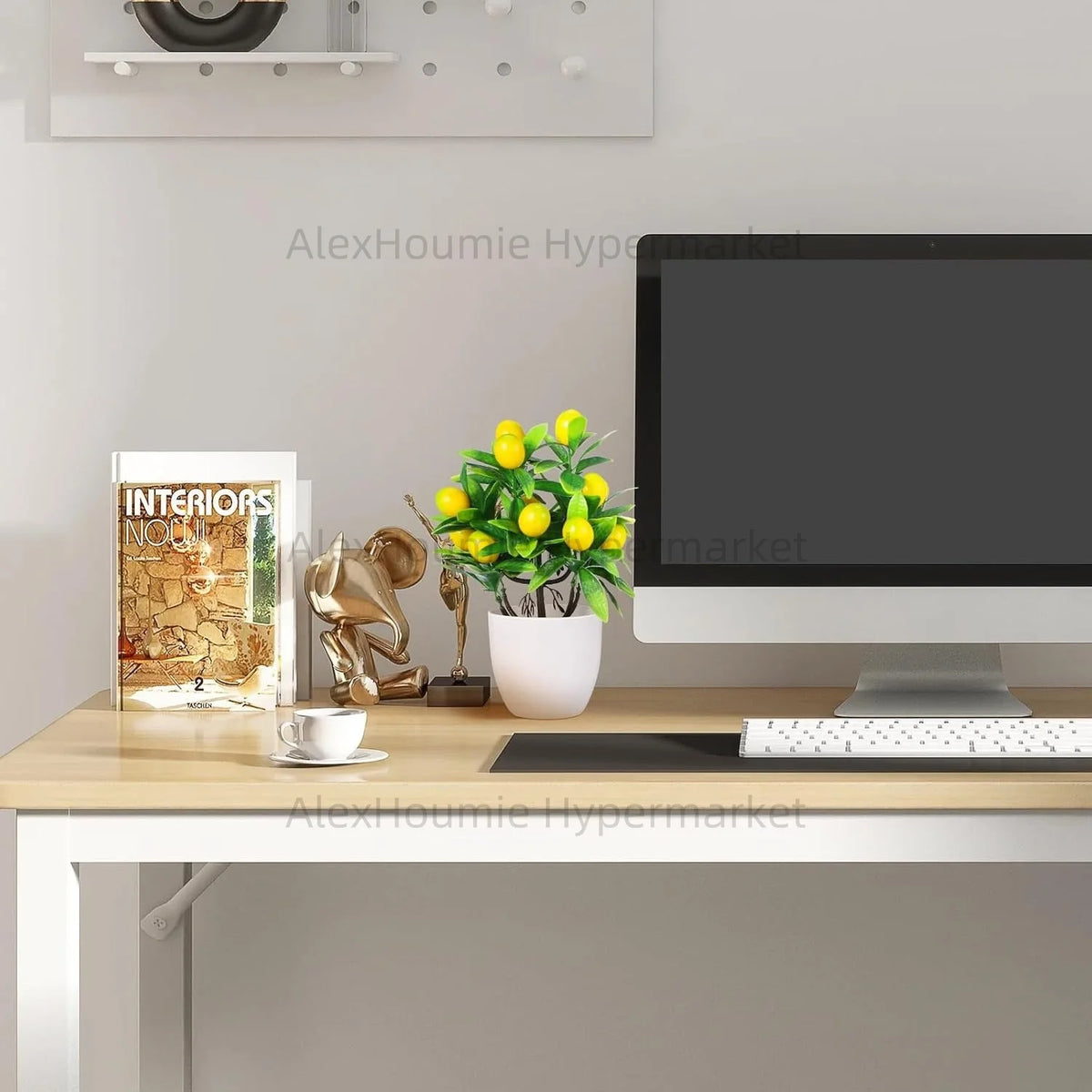 A small artificial lemon tree bonsai plant in a white pot sits on a wooden desk next to a computer monitor.