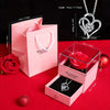 A pink gift box containing a preserved red rose and a silver heart-shaped necklace.