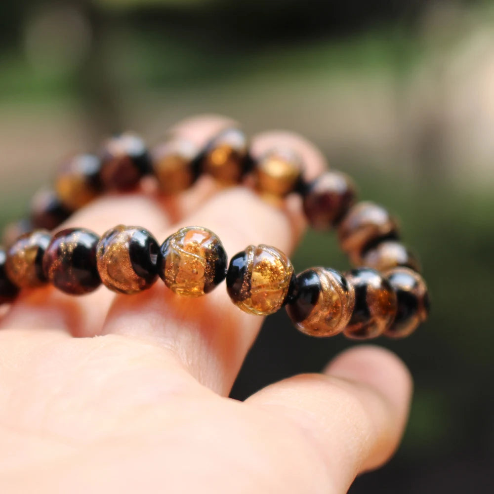 A hand holds a strand of handcrafted lampwork glass beads with gold accents against a blurred green background.