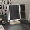 A triple fold LED makeup mirror with a light frame and a reflective surface is displayed on a dark surface.