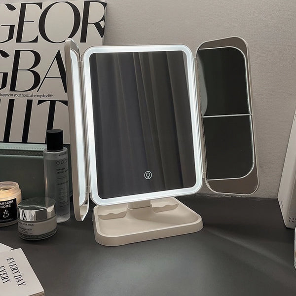 A triple-fold LED makeup mirror with adjustable panels is displayed on a dark surface.