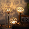 A set of three golden crystal candle holders with warm lights displayed on a dark surface.