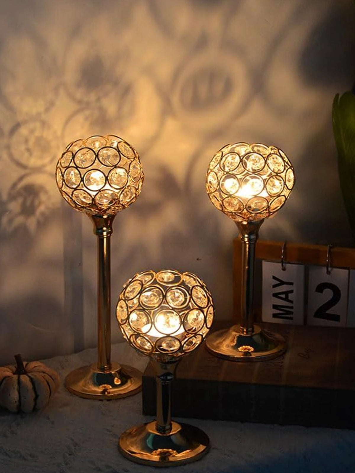 A set of three golden crystal candle holders with warm lights displayed on a dark surface.