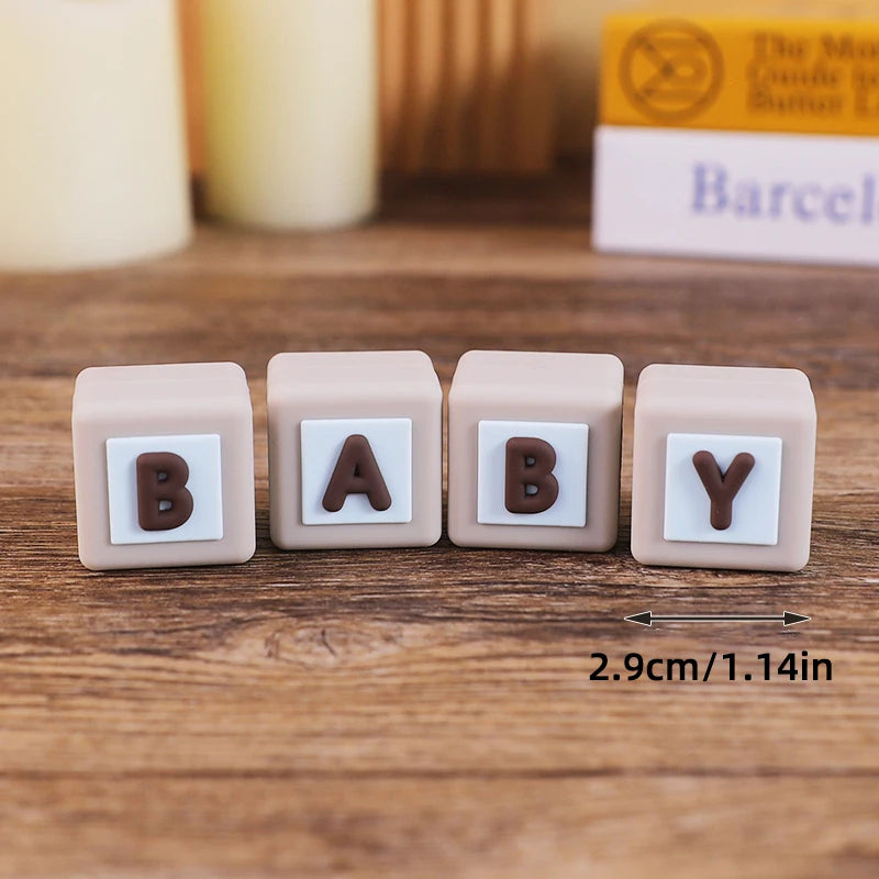 A set of five light pink baby blocks with the letters B A B Y in brown and white designs.