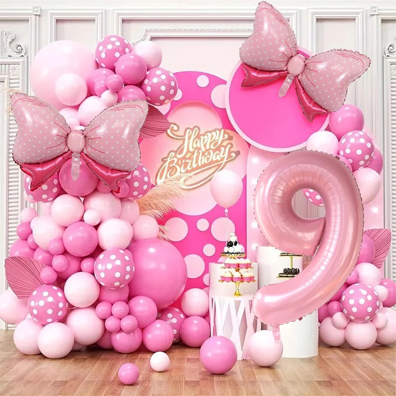A large pink and white balloon garland arch featuring various sized balloons and a large pink bow in a festive display.