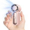 A hand holds a pink portable handheld cooling fan, demonstrating a strong stream of air.