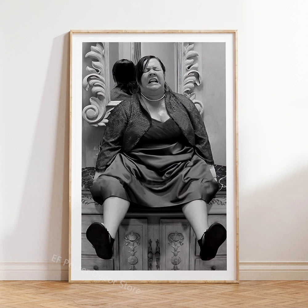 A black and white photograph of a woman with dark hair looking intensely, seated in front of an ornate mirror.