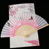 A vintage silk folding fan featuring pink and white floral patterns against a pale background.
