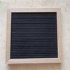 A rectangular wooden message board with a black, ribbed surface framed in light wood.