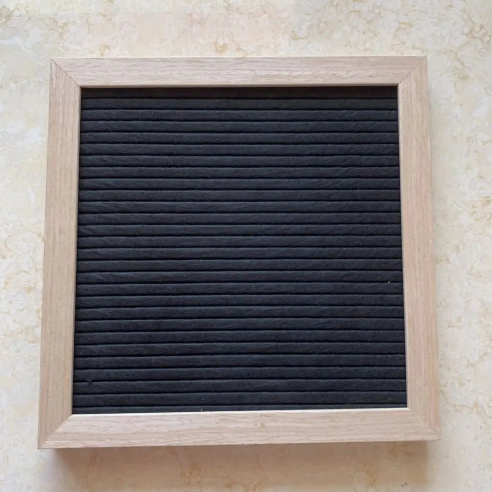 A rectangular wooden message board with a black, ribbed surface framed in light wood.