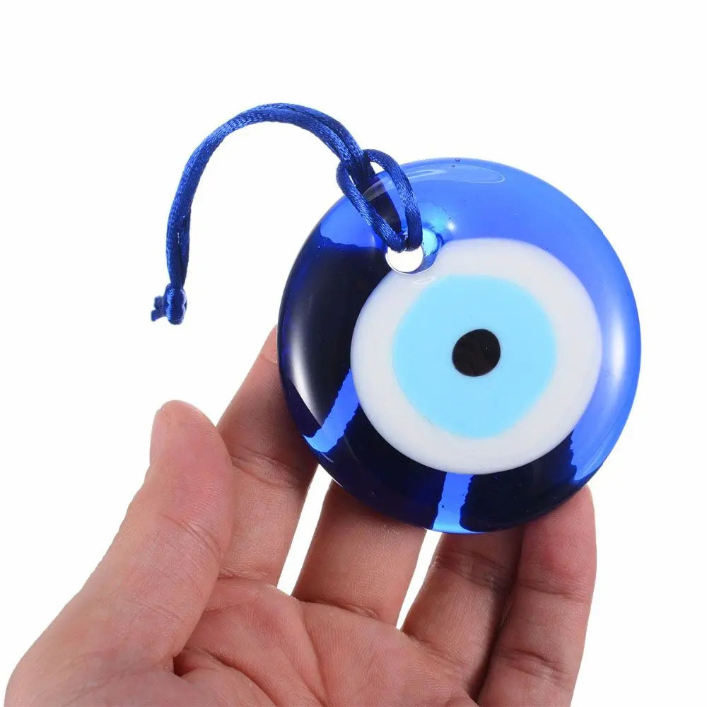 A blue glass evil eye amulet pendant with a white iris and blue string on a hand.