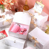 White gift box with pink items and gold ribbon ties displayed on a marble surface.