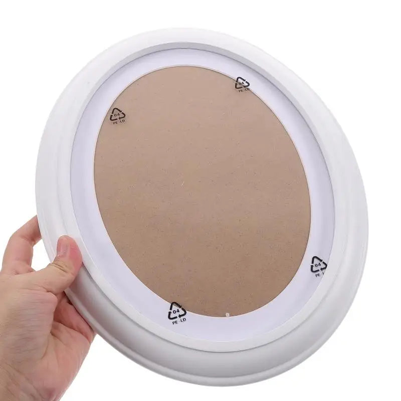 A white oval wooden wall photo frame with a light brown insert and small labels visible on the edge.