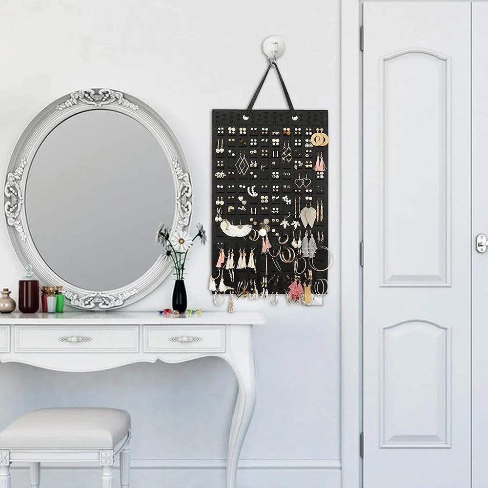 A black felt earring organizer display with various earrings hanging from a hanger mounted on a white wall.
