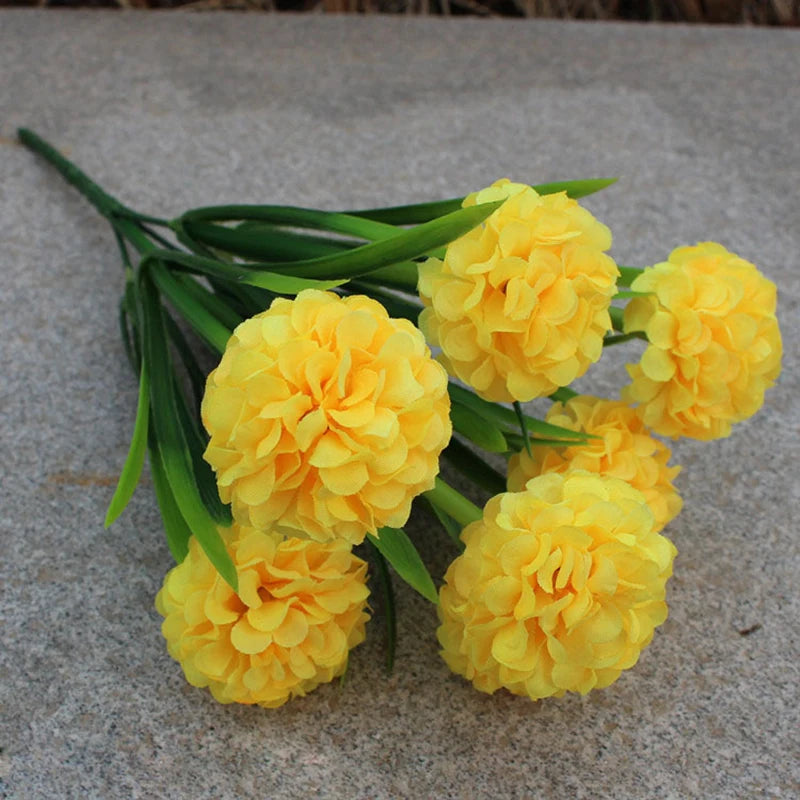 Un bouquet de fleurs artificielles d'hydrangea jaune vif avec des tiges vertes sur une surface grise.