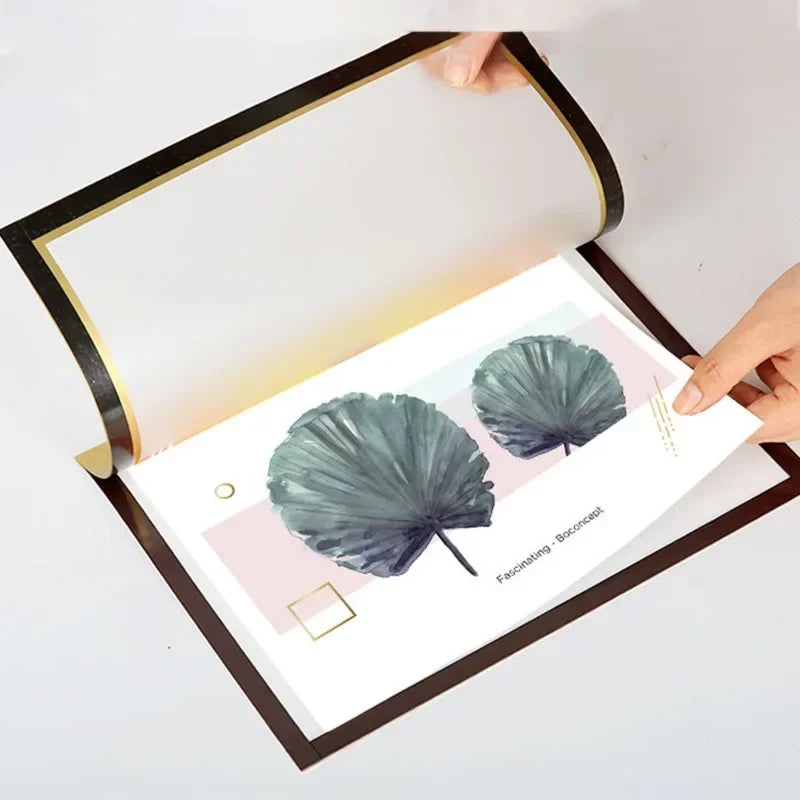 Eine Hand öffnet einen magnetischen Fotorahmen, der zwei grüne Monstera-Blätter auf weißem Hintergrund zeigt.