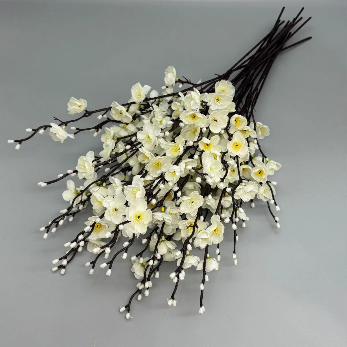 A bunch of white artificial plum blossoms on dark branches.