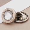 A close-up of a round, clear rhinestone button with a textured gold rim and a silver clasp.