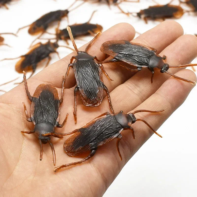 A hand holds several realistic plastic bugs including cockroaches, centipedes, and scorpions.