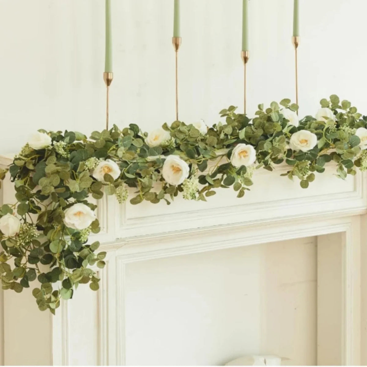 Eine Girlande aus künstlichen Eukalyptusblättern und weißen Rosen hängt über einem weißen Kaminsims.