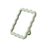 A light green wavy frame makeup mirror with a stand.