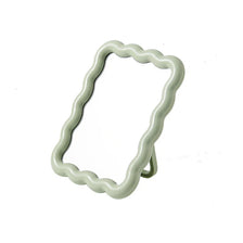 A light green wavy frame makeup mirror with a stand.
