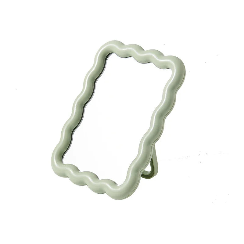 A light green wavy frame makeup mirror with a stand.