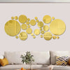 A collection of round gold 3D mirror decals displayed on a light wall above a sofa.