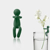 Three green human-shaped plant supports standing next to a glass of water.