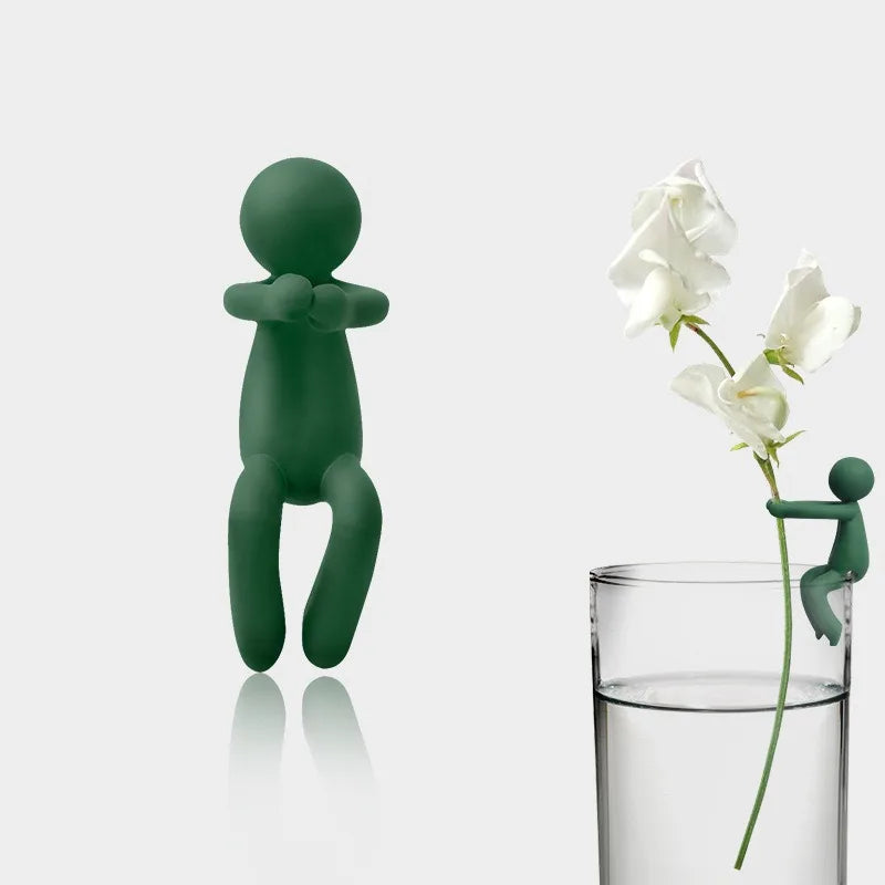 Three green human-shaped plant supports standing next to a glass of water.