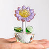 A handcrafted glass crystal sunflower figurine with a purple and yellow flower head and green leaves resting on a hand.