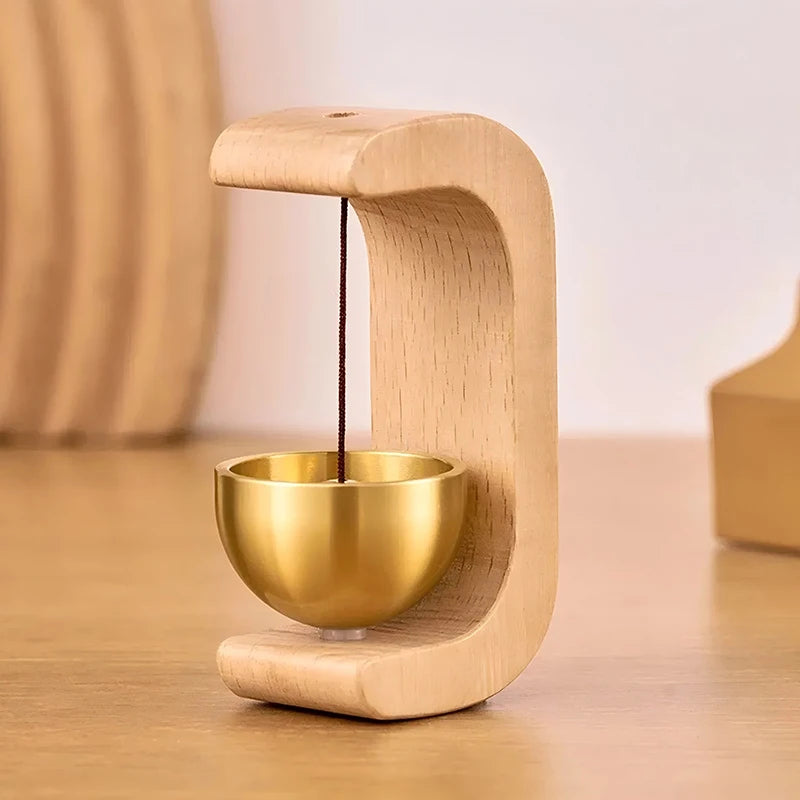 A light wood doorbell featuring a brass bowl and a thin dark cord, designed in an arched shape.